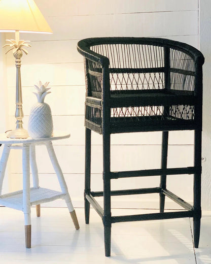 Black wicker bar stool in a room with a white wall and small table.