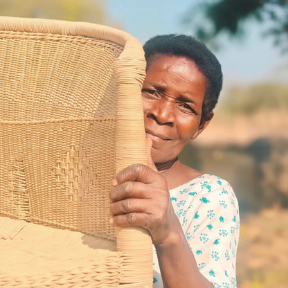 Woman holding a woven chair outdoors with a blurred natural background