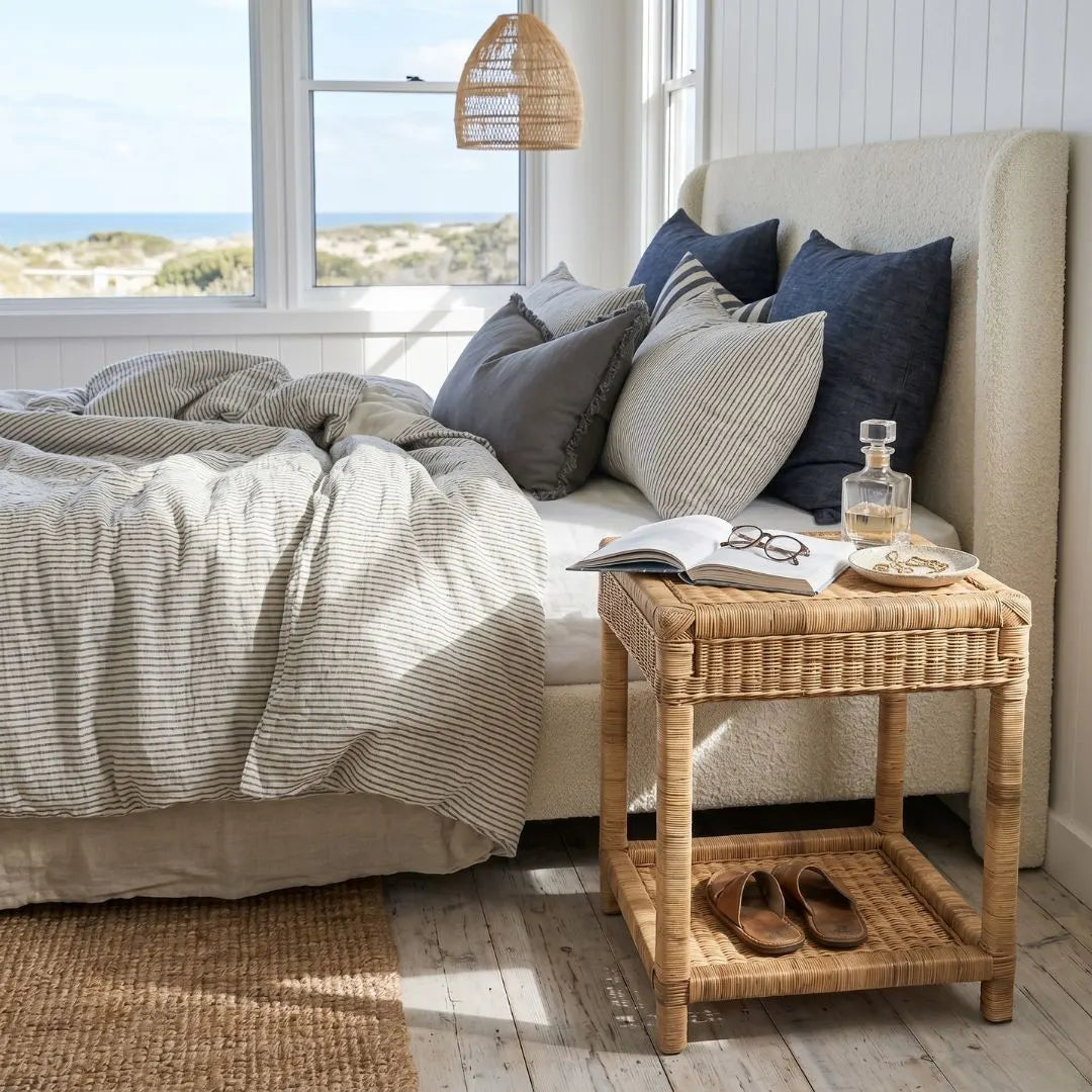 Cozy bedroom with a bed, pillows, and a wicker side table by a window with ocean view.