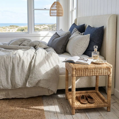 Cozy bedroom with a bed, pillows, and a wicker side table by a window with ocean view.