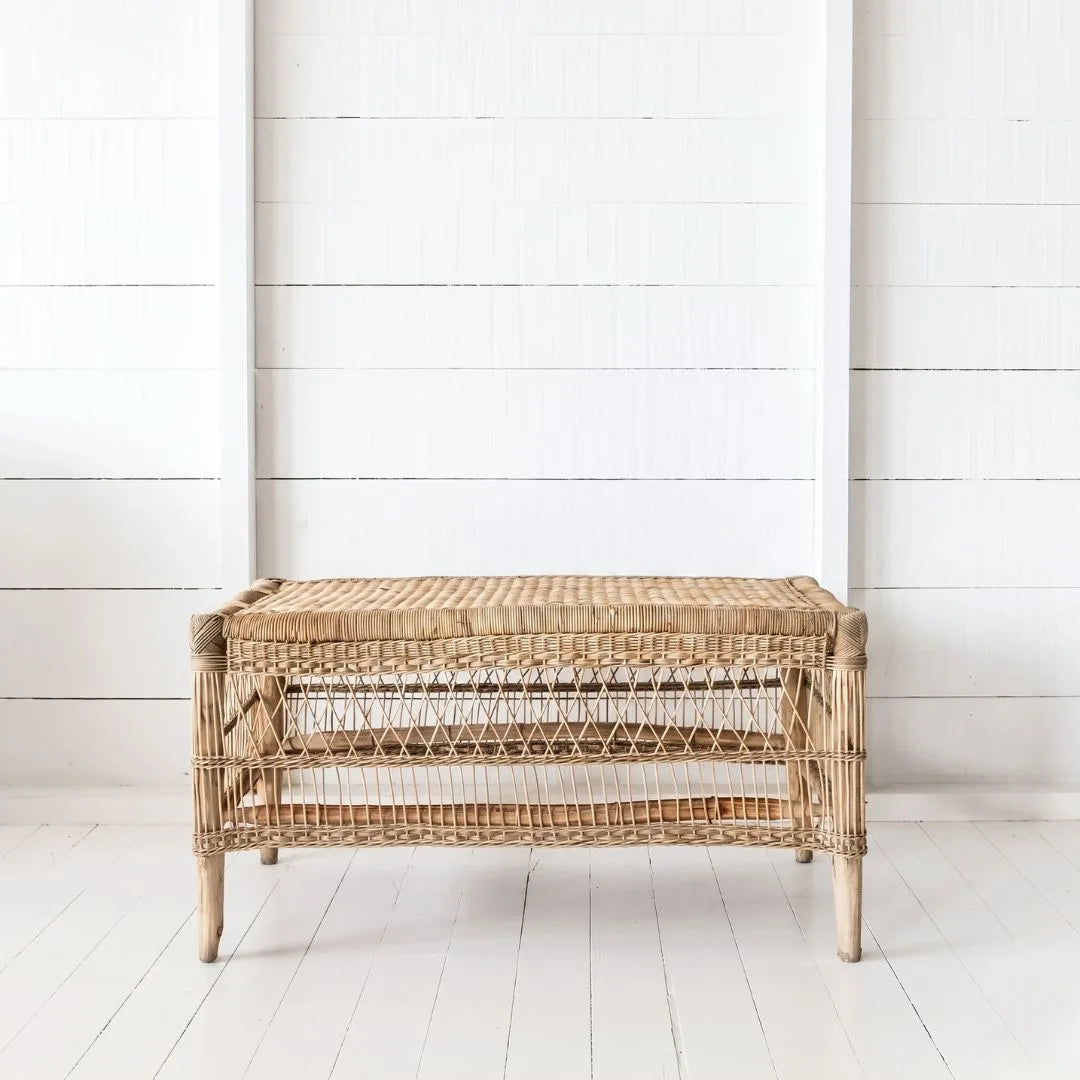 Wicker storage bench against a white wooden paneled wall.