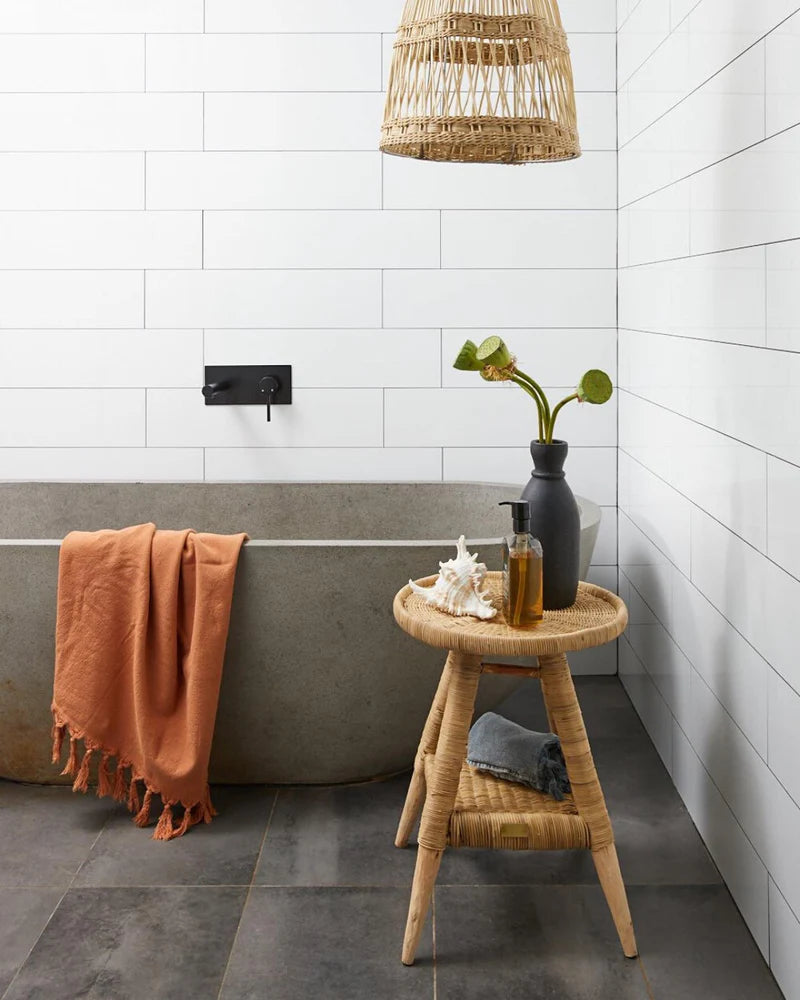 Bathroom with a bathtub, towel, and small table with a bottle and vase.