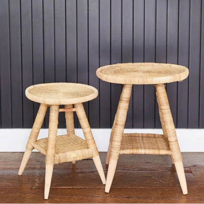 Two cane side tables against a dark paneled wall with a plant.