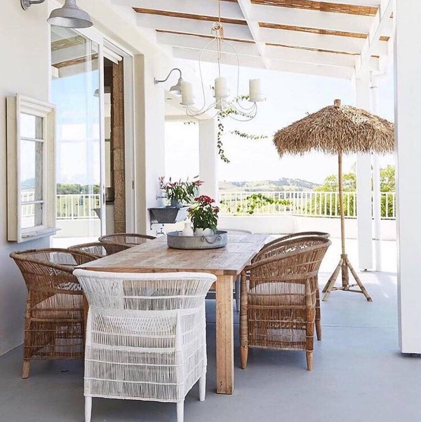 Outdoor patio with wooden table and malawi cane wicker chairs under a white pergola.