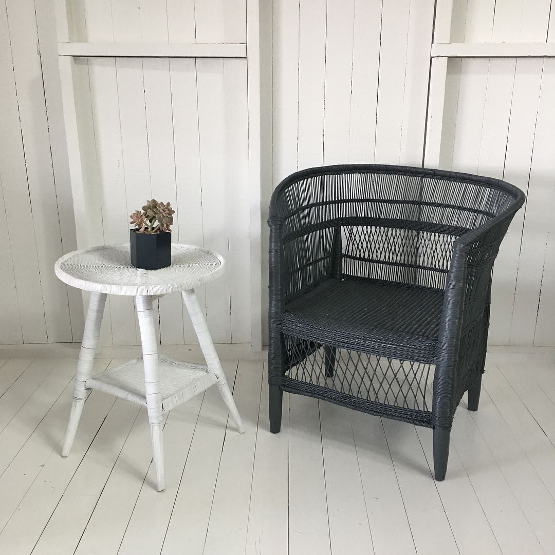 Black Malawi Cane chair and white side table with a plant against a white wooden wall.
