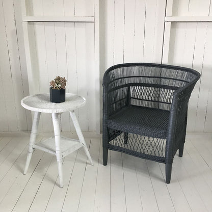 Black Malawi Cane chair and white side table with a plant against a white wooden wall.