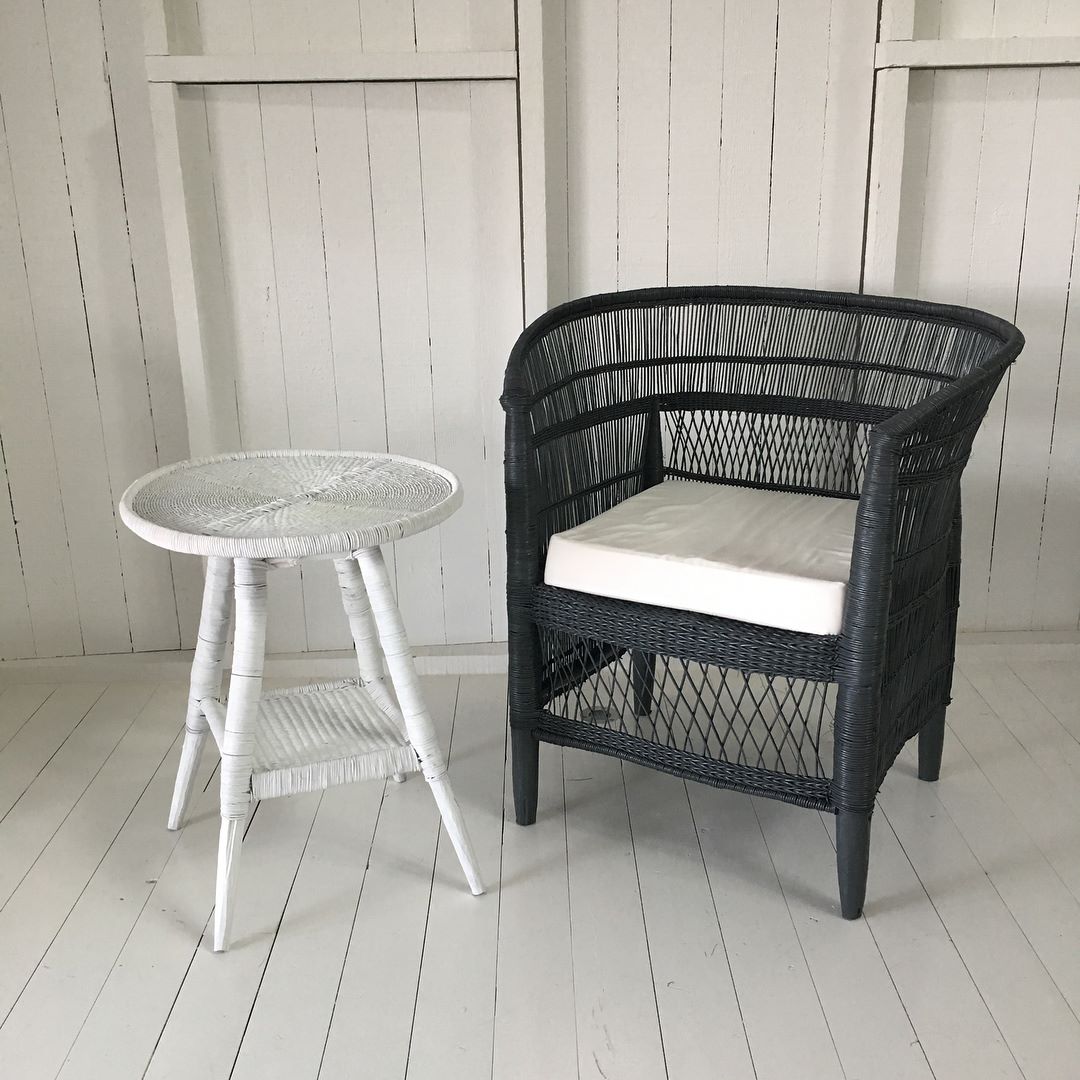 Black Malawi Cane chair with white cushion next to a white side table against a wooden paneled wall.