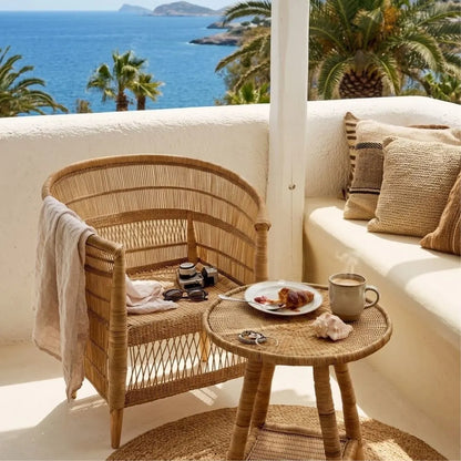 Balcony with wicker chair, table, and sofa with pillows overlooking the ocean.