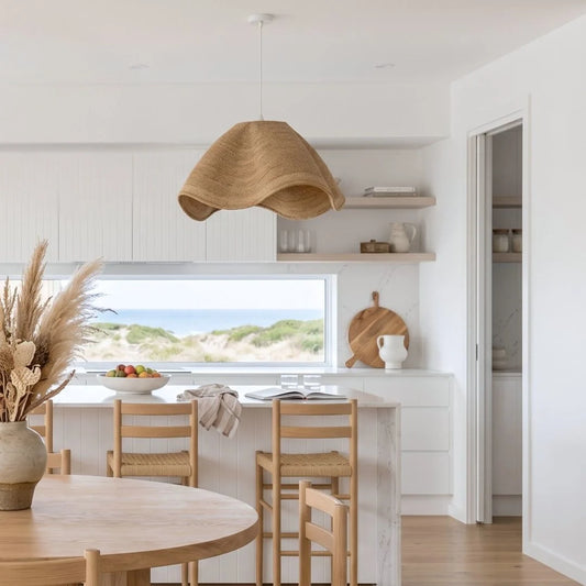 Modern kitchen with wooden dining table and chairs, wicker pendant light, and view of beach.