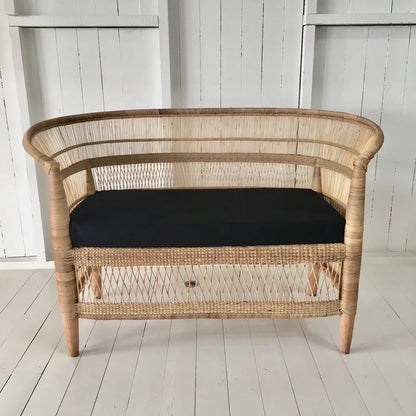Wicker loveseat with a black cushion on a white wooden floor.