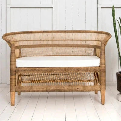 Wicker chair with white cushion next to a potted plant on a white wooden floor.