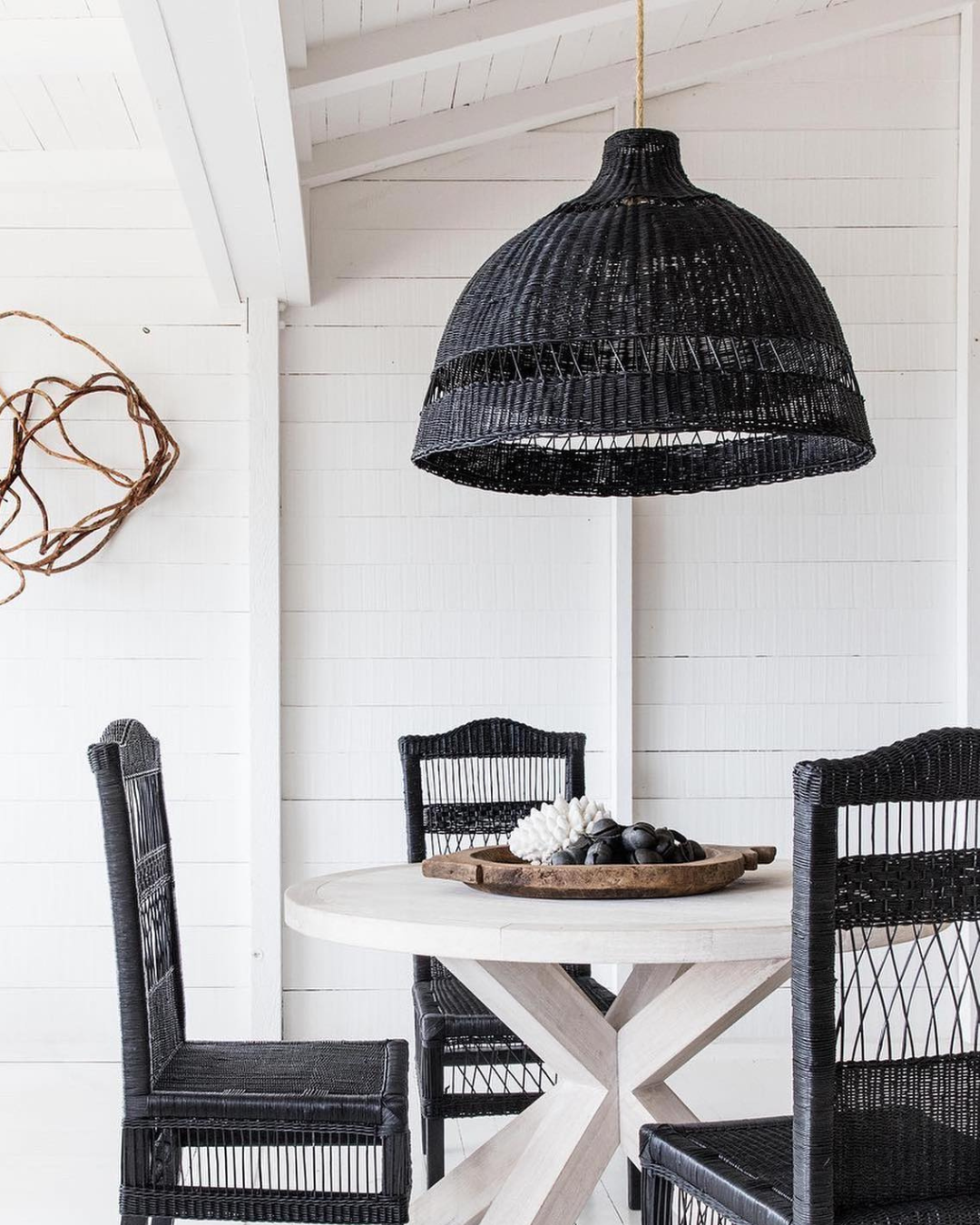 Black woven pendant light hanging above a dining table with chairs in a bright room.