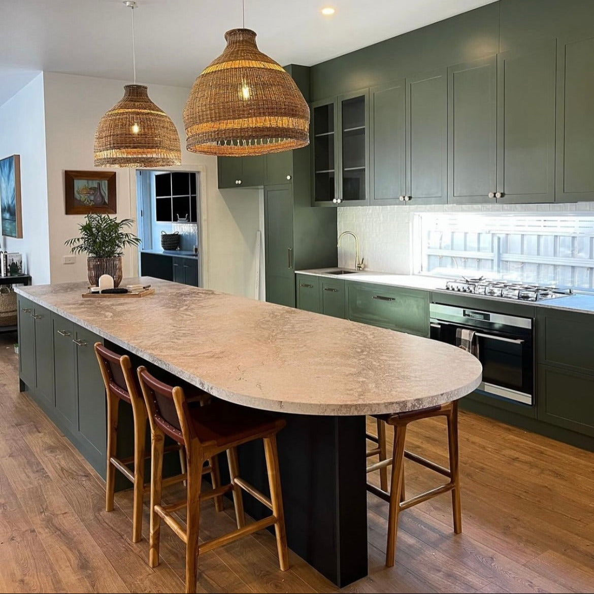 Modern kitchen with green cabinets, a stone island, and wooden stools.