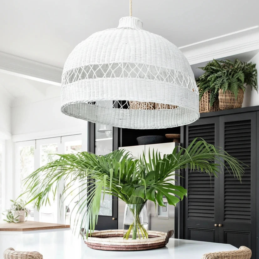 White woven pendant light fixture in a room with plants and furniture.