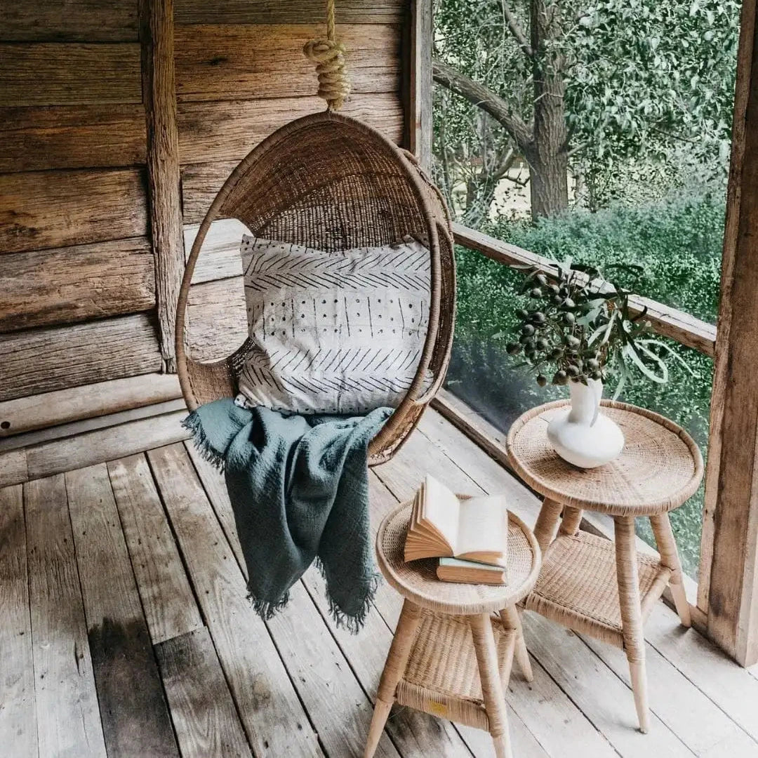 Wooden hanging chair with cushions on a rustic wooden deck with a view of trees.
