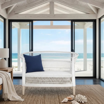 White wicker chair with a blue pillow in a room with large windows overlooking the ocean.