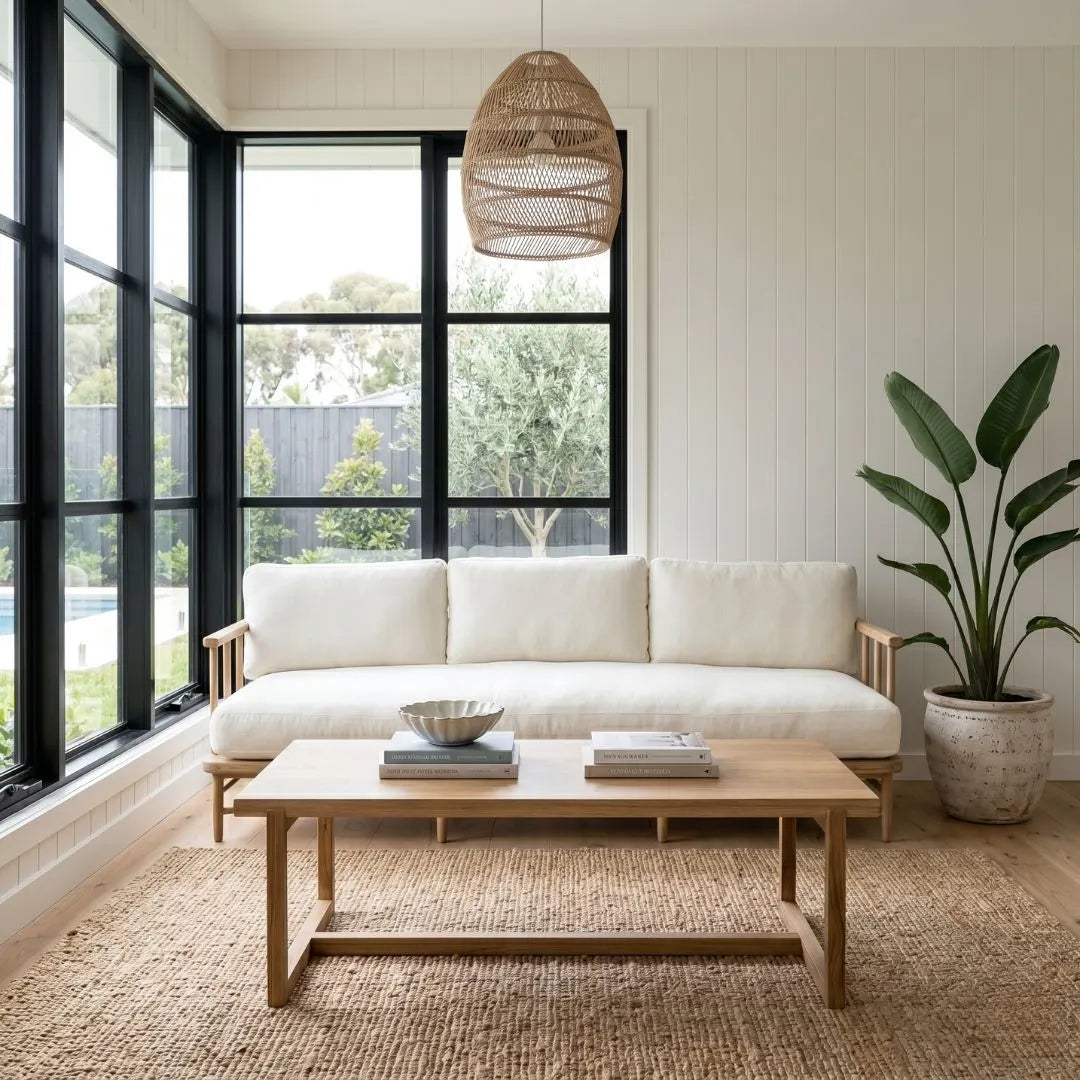 Modern living room with a white sofa, wooden coffee table, and large windows.