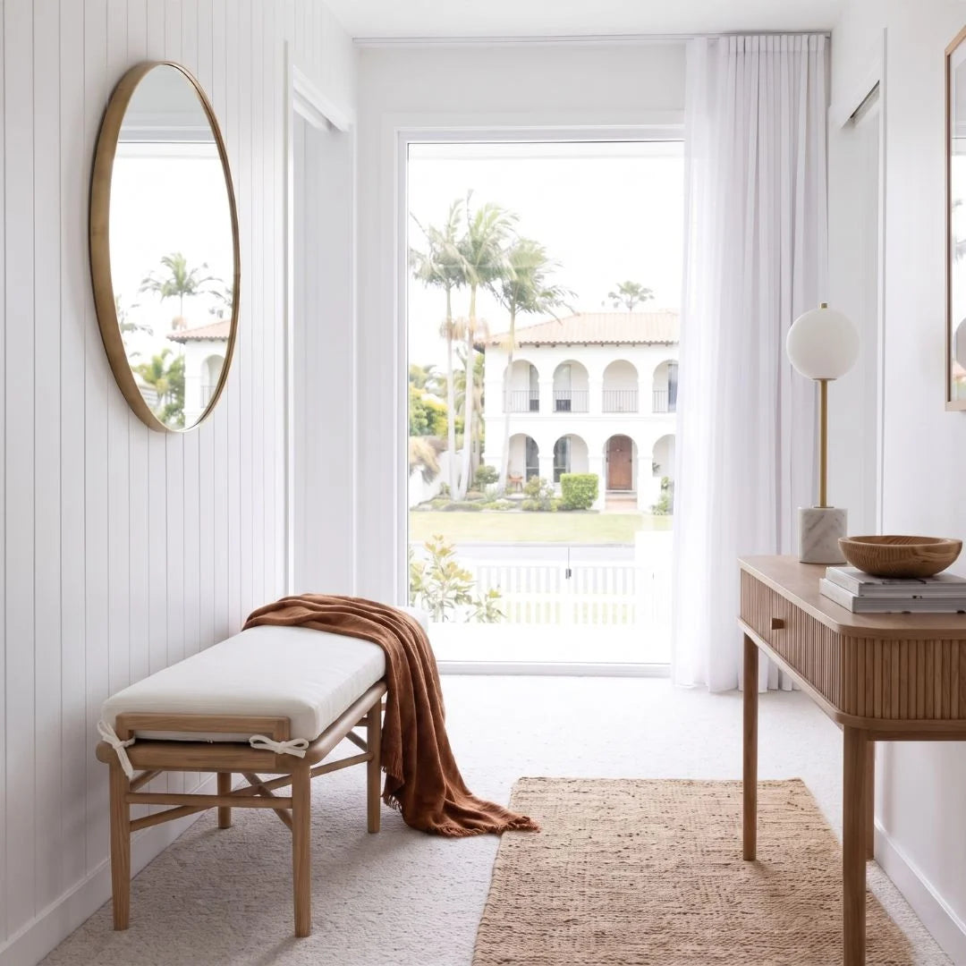 Modern interior with a bench, mirror, and table in a bright room with a view of a garden.