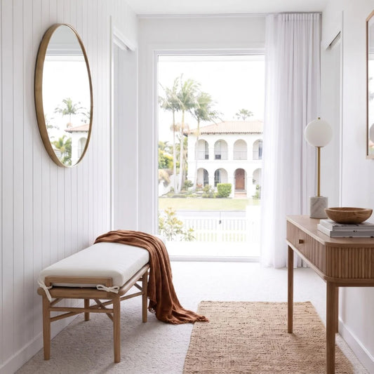 Modern interior with a bench, mirror, and table in a bright room with a view of a garden.