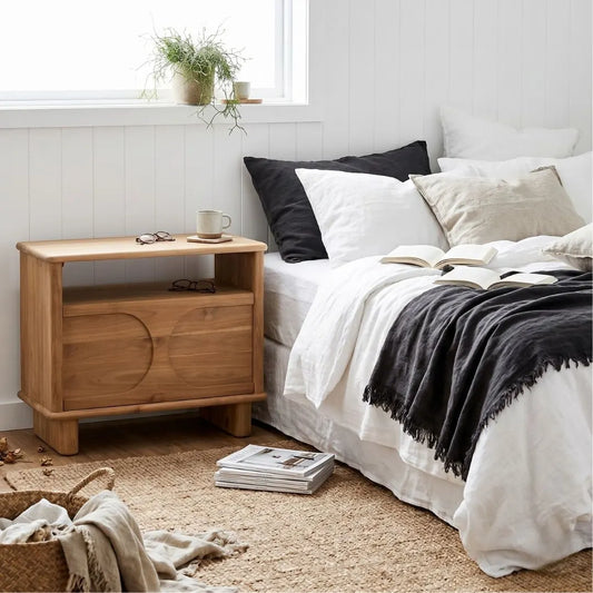 Bedroom with Mea teak nightstand, bed with pillows, and books from Sun Republic
