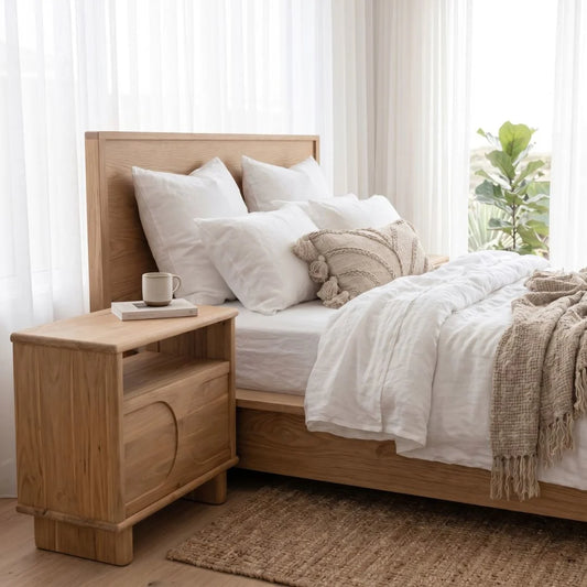 Neatly made bed with mea teak nightstand in a bright bedroom.