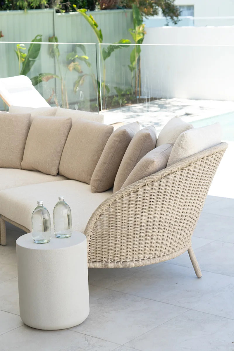 Beige outdoor sofa with wicker armrest and a small round table on a patio.