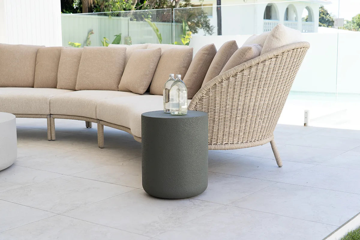 Beige outdoor sofa with wicker chair and deep moss green side table on a patio