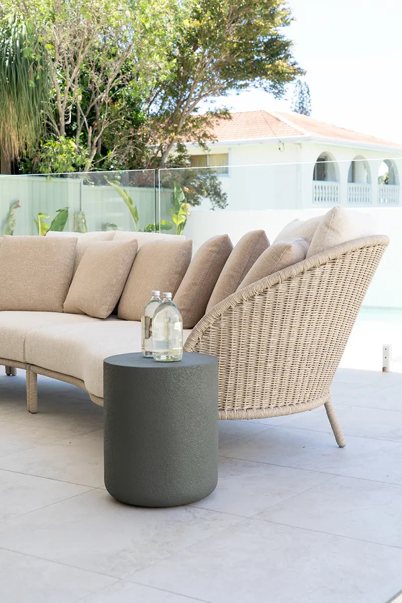 Outdoor patio setting with a beige sofa, wicker chair, and gray side table.