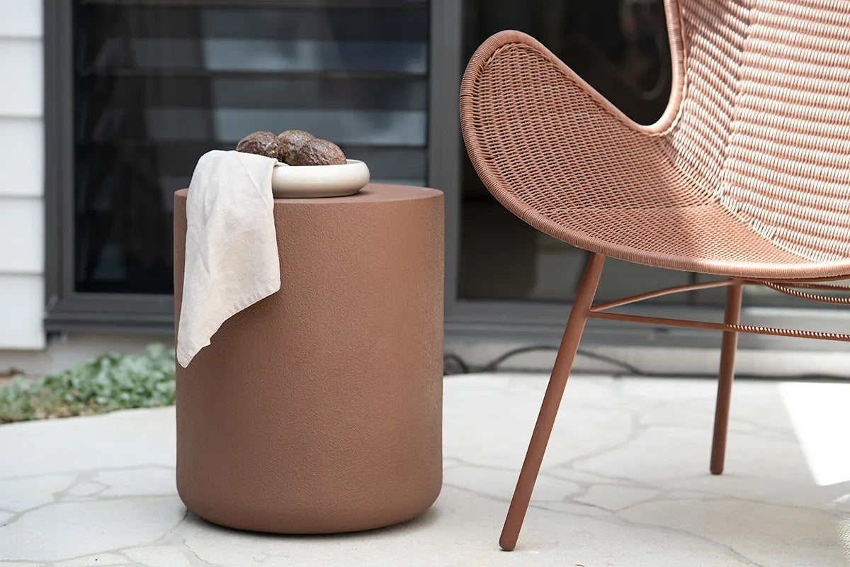 Brown cylindrical container with a white towel on a patio next to a wicker chair.