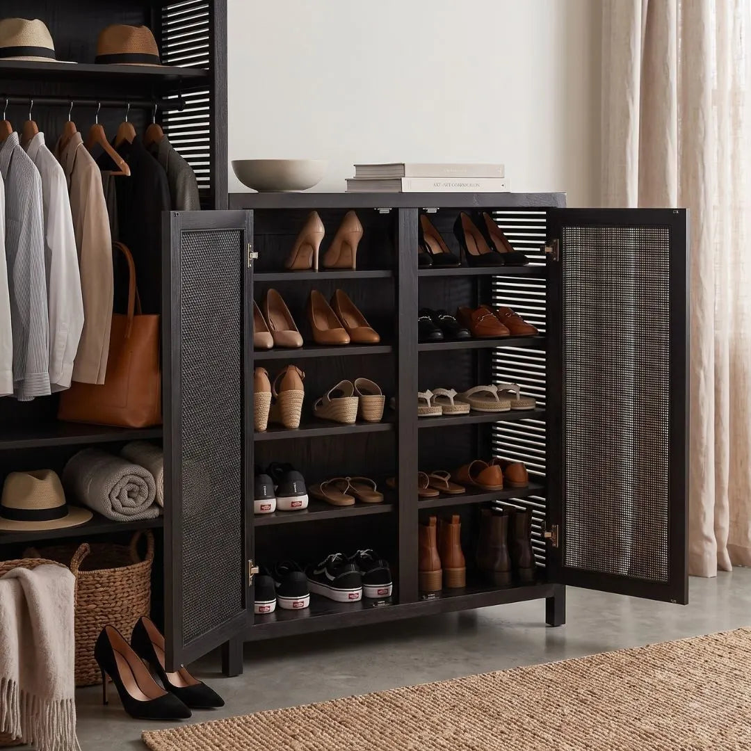 A tall black shoe cabinet with two open doors, shown in a styled entryway. The cabinet has multiple shelves with various shoes and is flanked by a matching black shelving unit on the left containing folded clothes, hats, and a tote bag, and a beige curtain on the right.