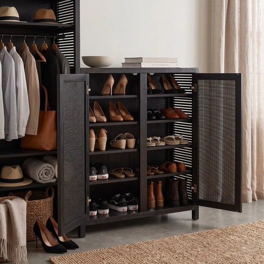 A tall black shoe cabinet with two open doors, shown in a styled entryway. The cabinet has multiple shelves with various shoes and is flanked by a matching black shelving unit on the left containing folded clothes, hats, and a tote bag, and a beige curtain on the right.
