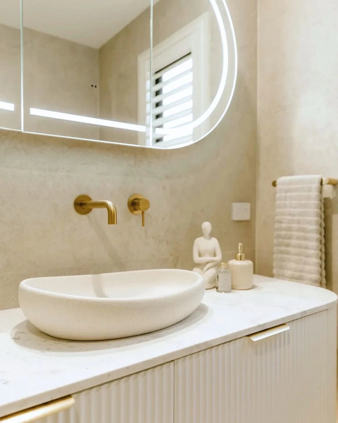Modern bathroom with a white sink, gold faucet, and illuminated mirror.