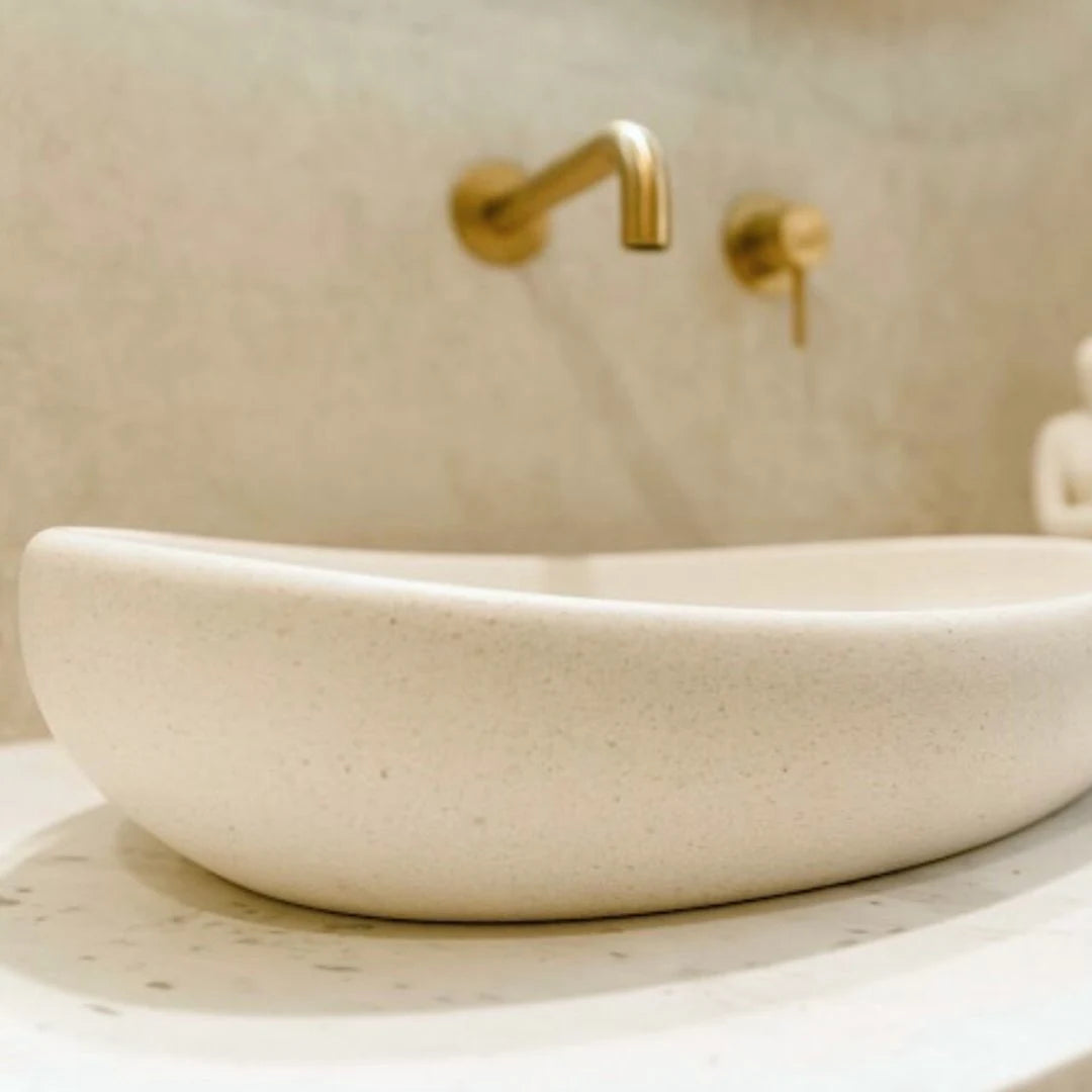 Beige stone sink with gold faucet in a bathroom setting