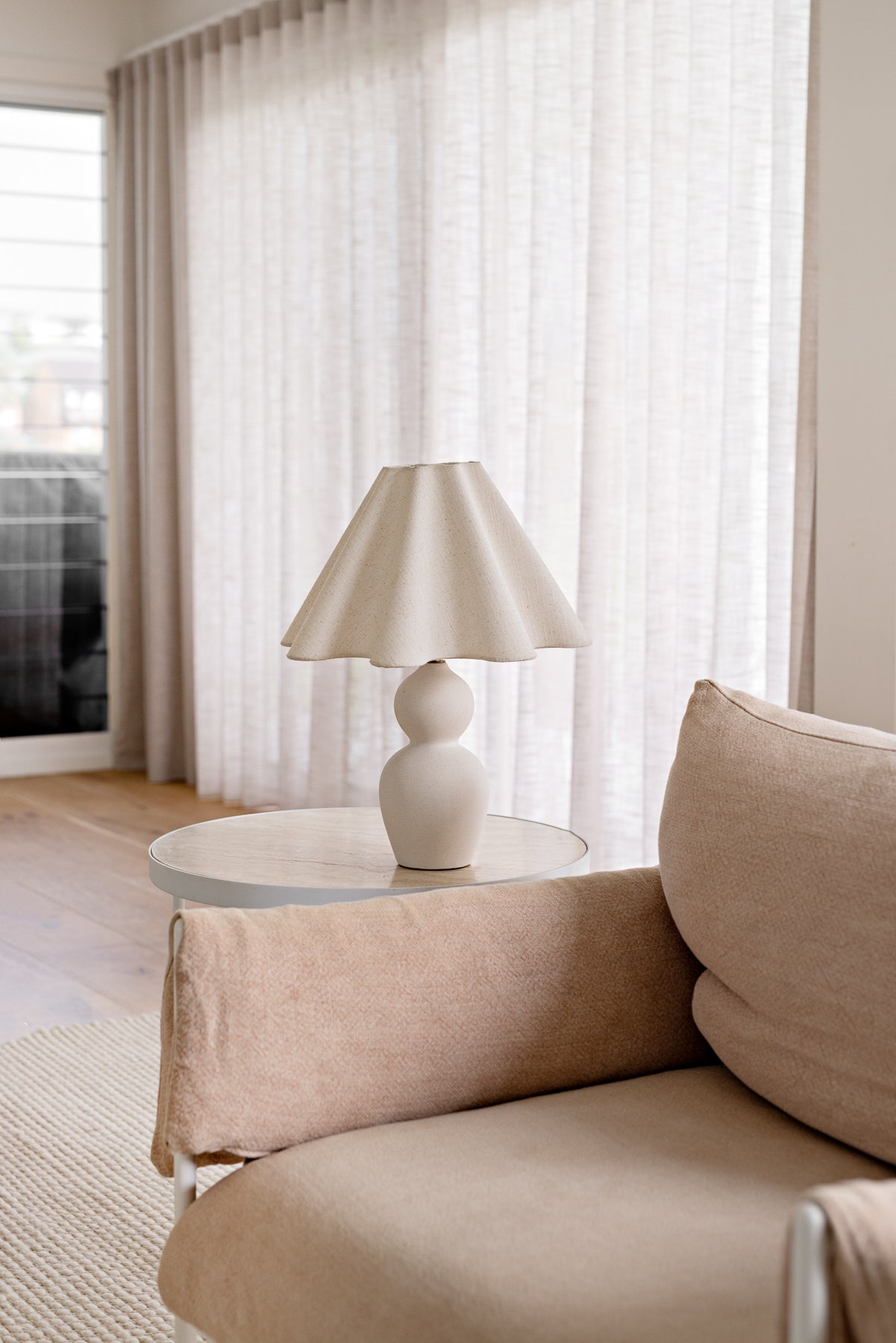 Beige sofa with a lamp on a small round table in a room with light curtains.