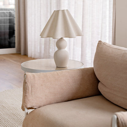 Beige sofa with a lamp on a small round table in a room with light curtains.