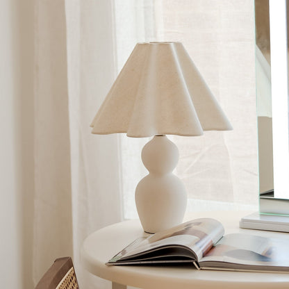 White table lamp on a side table with a magazine against a window with sheer curtains