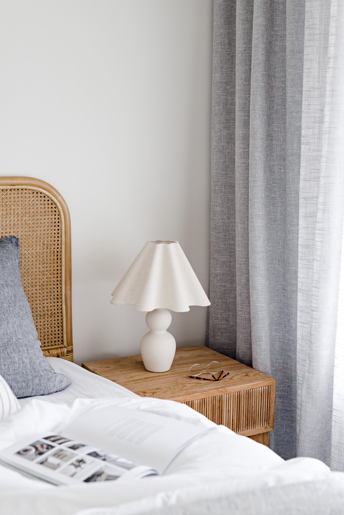 Bedroom with wicker headboard, white bedding, and a lamp on a wooden nightstand.