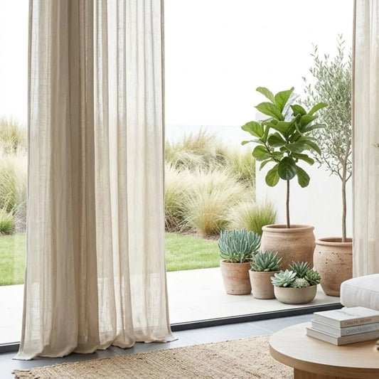 Living room with large windows, white curtains, and various potted plants.