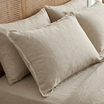 Beige pillows with frayed edges on a bed with a wicker headboard.