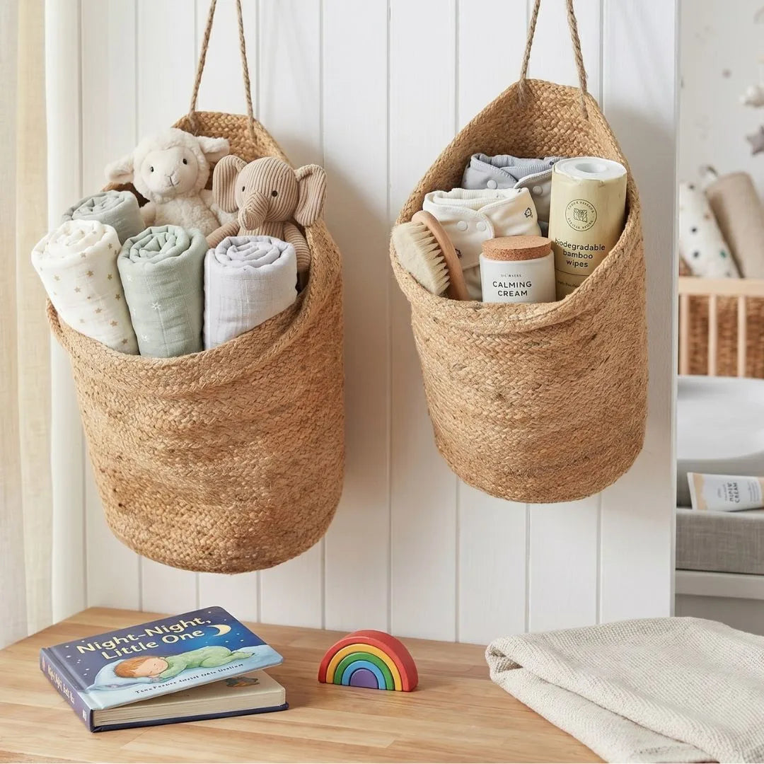 Two woven baskets hanging on a wall with baby items inside, in a room setting.