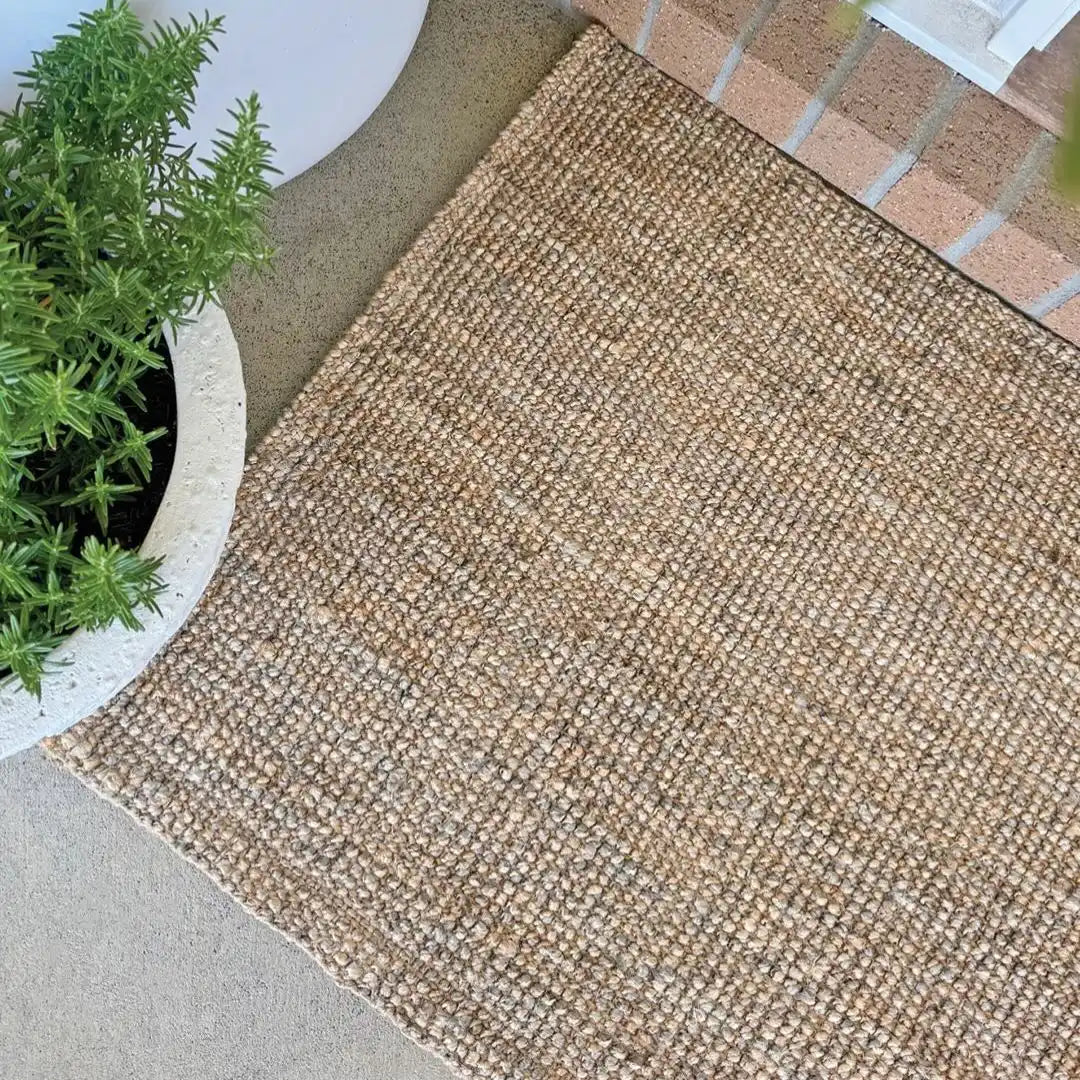 Textured beige mat on a concrete surface with a plant in the corner