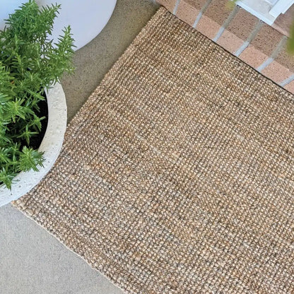 Textured beige mat on a concrete surface with a plant in the corner