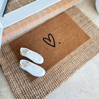 Doormat with a heart design and two white shoes on a concrete floor.