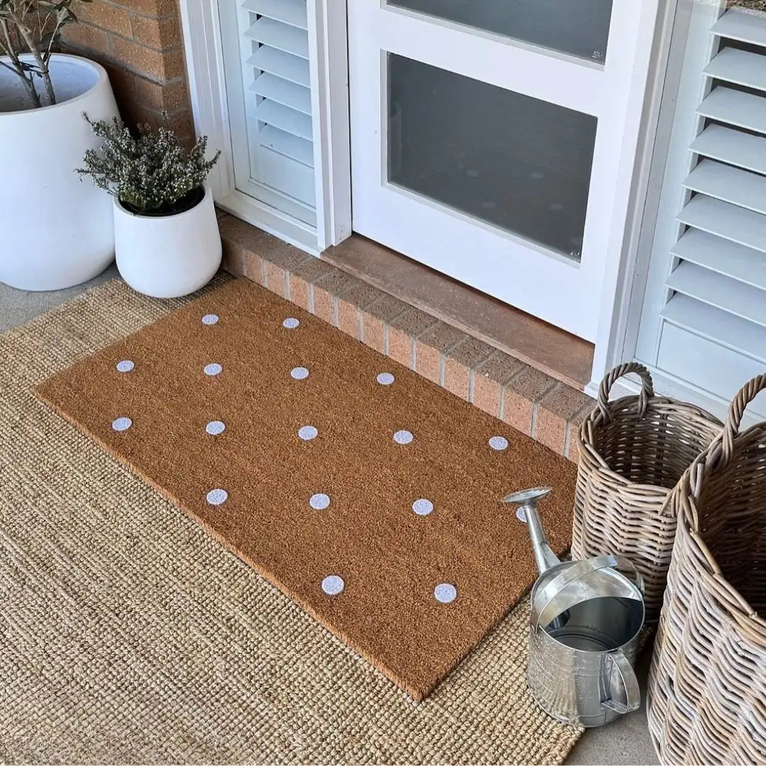Doormat with white polka dots on a textured surface near a door.