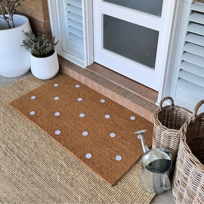Doormat with white polka dots on a textured surface near a door.