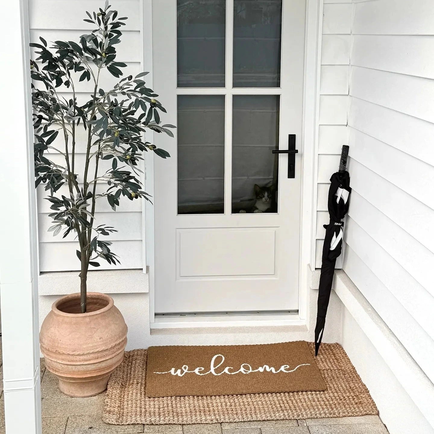 Front door of a house with a 'welcome' mat, plant, and umbrella on a white porch.