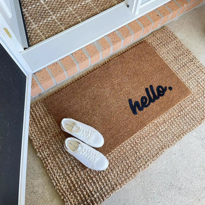 Doormat with 'hello' text on a threshold between indoor and outdoor areas.
