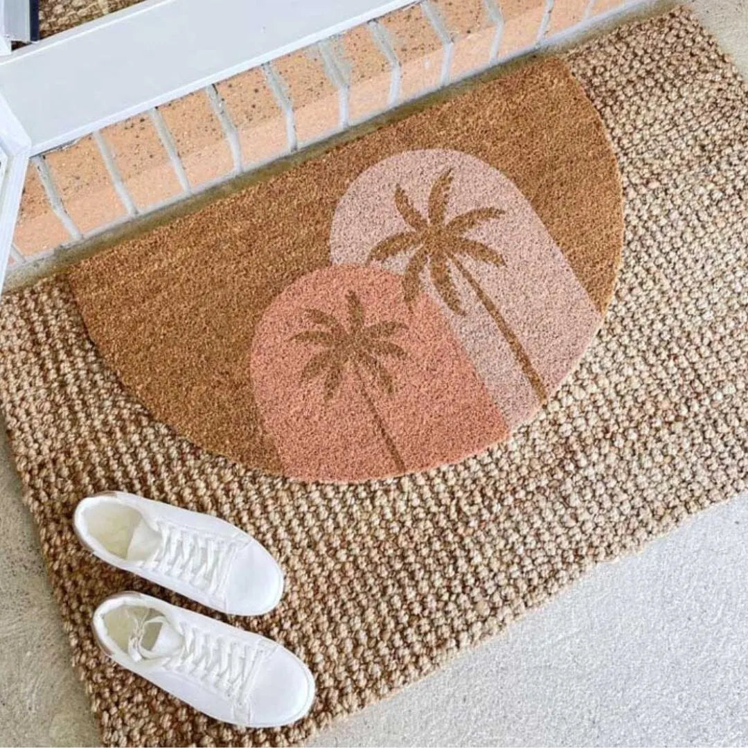 Doormat with palm tree design on a brick surface, with white sneakers in front.