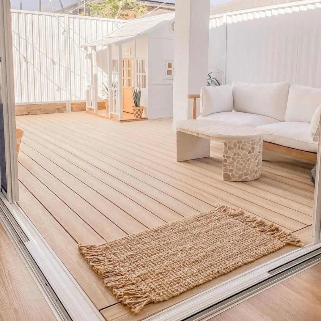 Wooden deck with a woven jute mat, white sofa, and decorative elements.
