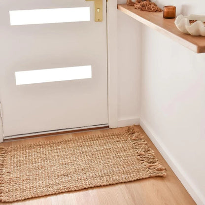 Jute rug on a wooden floor in front of a white door with a wooden shelf above.